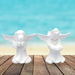 2 unpainted ceramic angel dogs standing on a wooden deck by the ocean.